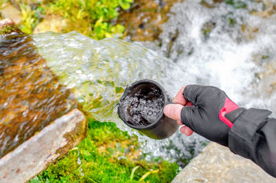 The flow of pure spring water. a man's hand collects water in mug in crystal cool spring.