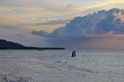 Silhouette people on sea against sky during sunset