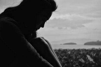 Side view of sad woman sitting by glass window