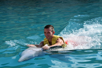 Young man holding dolphin in sea