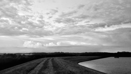 Road passing through field against cloudy sky