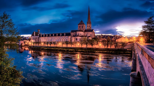 Illuminated buildings by river against sky at night