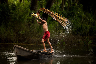 Full length of shirtless boy standing on boat in water