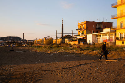 Man walking on street against buildings in city at sunset