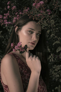 Portrait of beautiful woman with pink flower against plant