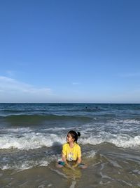 Smiling girl sitting at shore against sky