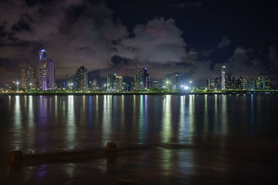 Illuminated city by sea against sky at night