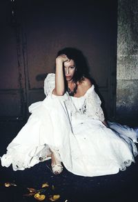 Portrait of sad young woman in gown sitting by door at night