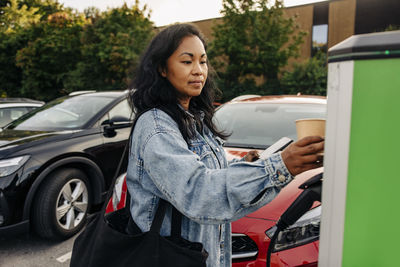 Woman wearing denim jacket operating kiosk at charging station