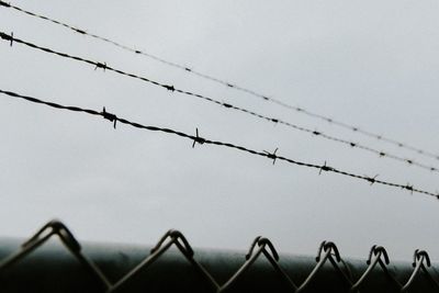 Low angle view of barbed wire fence against sky