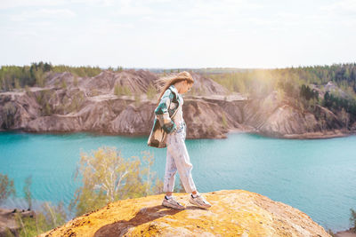 Rear view of woman standing on rock by lake