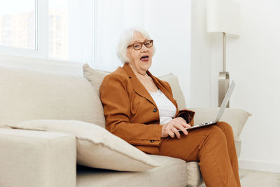 Senior woman with laptop sitting on sofa at home