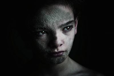 Close-up of boy face covered with sand against black background