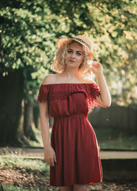 Portrait of beautiful young woman wearing hat and red dress standing in park