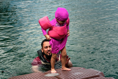 Full length portrait of happy girl in pink swimming suit with father in water.