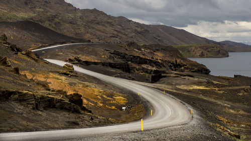 Winding road on mountain against cloudy sky