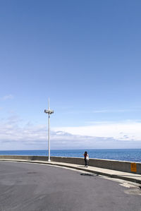 Woman walking on promenade by sea against blue sky