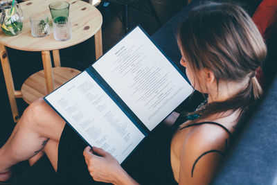 High angle view of young woman reading menu while sitting on sofa at cafe