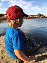 Boy sitting on lakeshore against sky