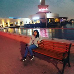 Full length portrait of woman sitting on illuminated street at night