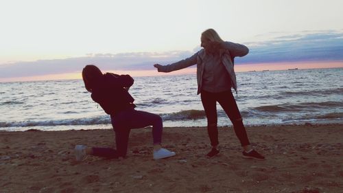 Full length of friends standing on beach against sky during sunset