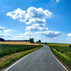 Empty road amidst field against sky