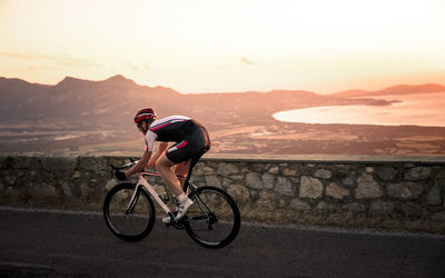 Man riding bicycle on road against mountains and sky during sunset