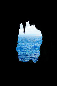 Silhouette rock formation in sea against sky