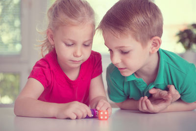 Cute smiling sibling playing with dice on table at home