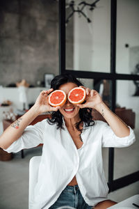 Smiling woman holding grapefruit while sitting at home