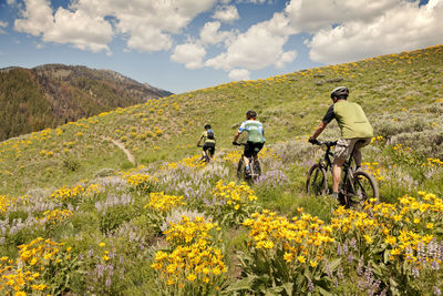 Friends riding bicycle on hill against cloudy sky