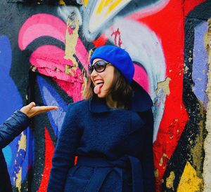 Cheerful woman sticking out tongue against colorful graffiti wall