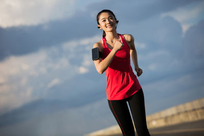 Smiling young woman running on road against cloudy sky during sunset