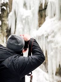 Side view of man photographing frozen waterfall