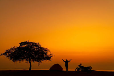 Silhouette people riding bicycle against orange sky