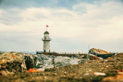 Lighthouse amidst buildings and sea against sky