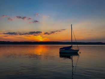 Sailboats moored on sea against sky during sunset