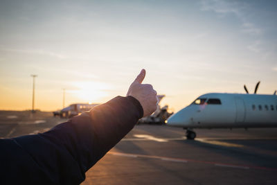 Member of ground crew showing thumbs up to airplane. traffic at airport during sunset.