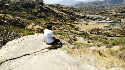 Rear view of man sitting on mountain against sky