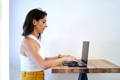 Side view female freelancer in summer outfit typing on laptop at table in cafe while teleworking on project