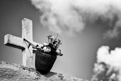 Flowerpot hanging from a cross at a cemetery with sky and clouds