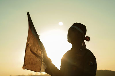 Silhouette man holding flag against clear sky during sunset