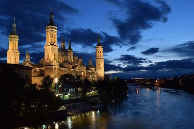 River amidst illuminated buildings against sky at dusk