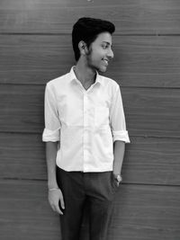 Young man looking away while standing against wooden wall