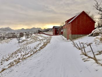 Snow covered field by buildings against sky during winter