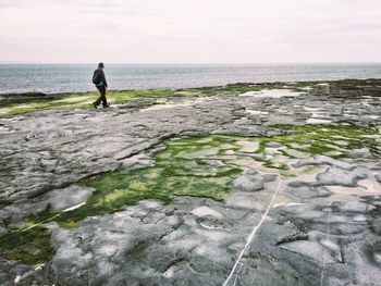 Man walking on sea shore against sky