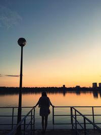 Silhouette woman photographing river against sky during sunset