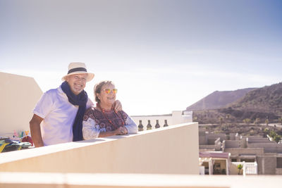 Smiling couple standing on terrace against sky