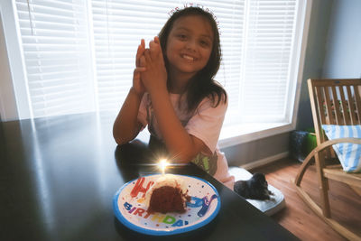 Portrait of smiling girl sitting by cake at home