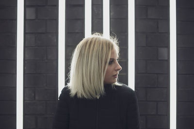 Close-up woman looking away while standing against illuminated lights on wall